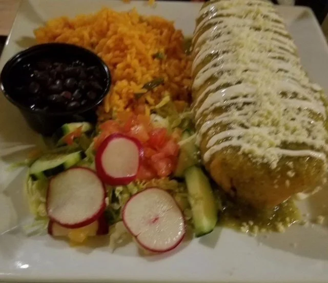 Plate of Mexican food including burrito, rice, black beans, and salad with radish slices and cucumber.