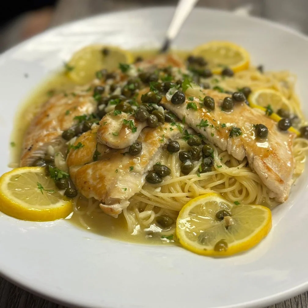 Lemon pepper chicken served over spaghetti with capers and lemon slices garnished with parsley.