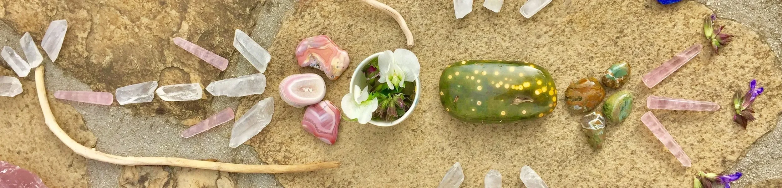 Arrangement of various colorful stones, shells, and a small white pot with white flowers on a beige rocky surface.