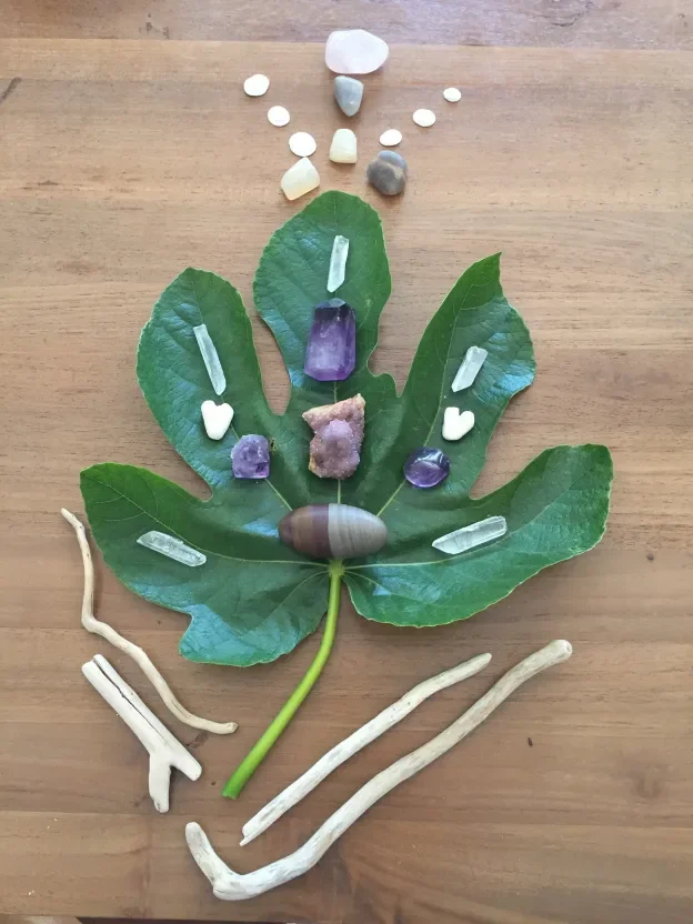 Leaf with various crystals and stones arranged on and around it to create a butterfly shape, placed on a wooden surface.