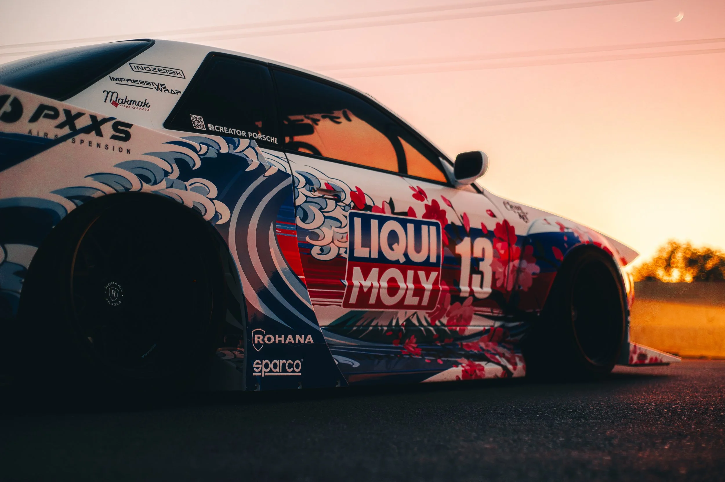 Race car in colorful graphics with sponsor logos, captured at sunset, side view, on track.