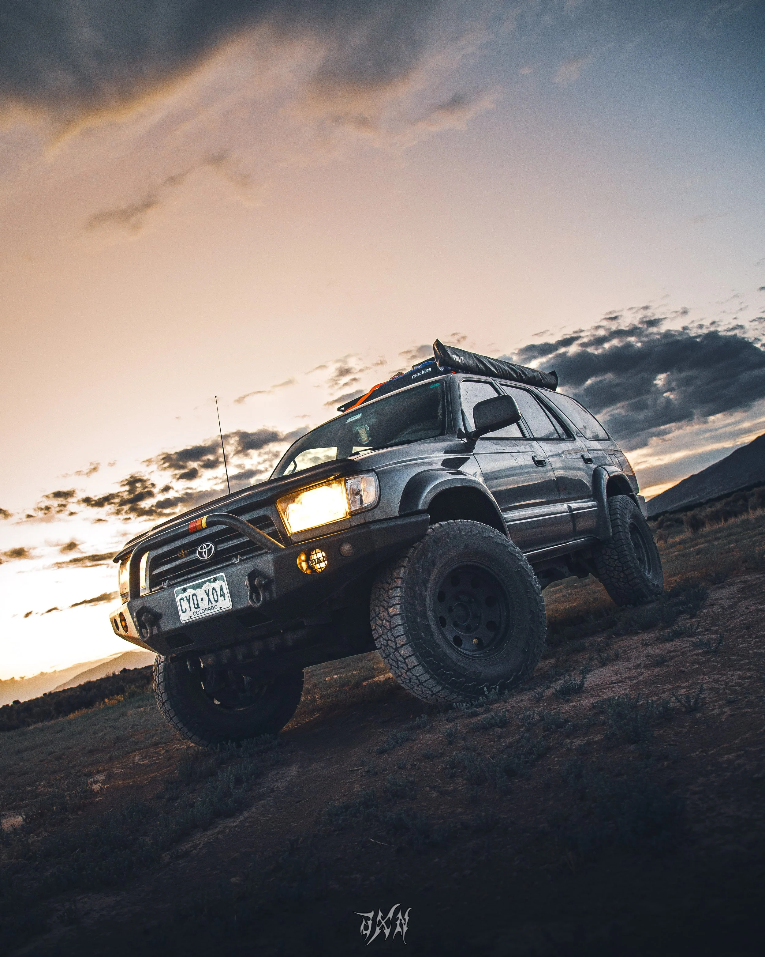 A black off-road SUV parked on a dirt terrain during sunset with clouds in the sky.