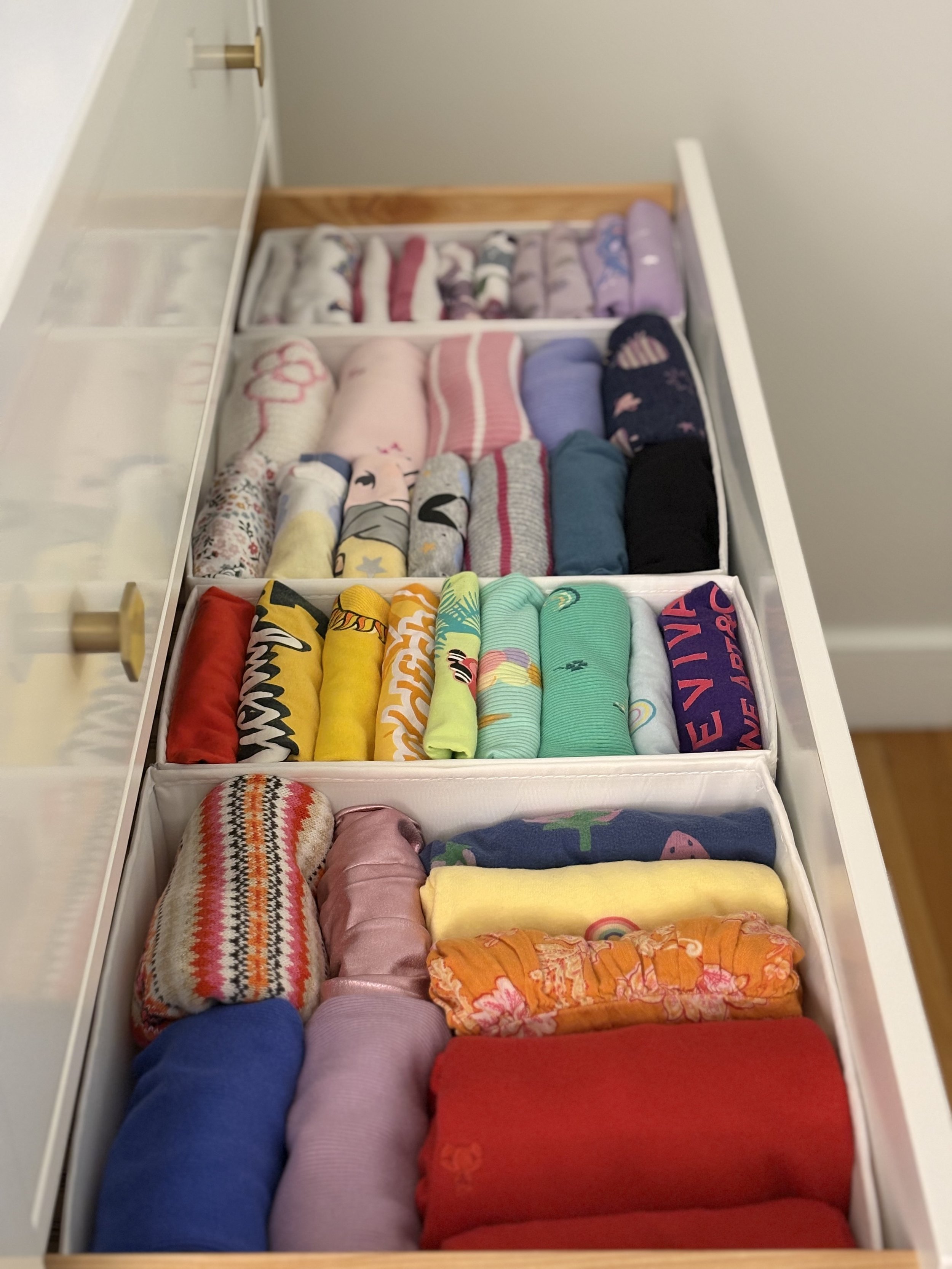 A drawer filled with neatly folded, colorful clothing organized in separate compartments.