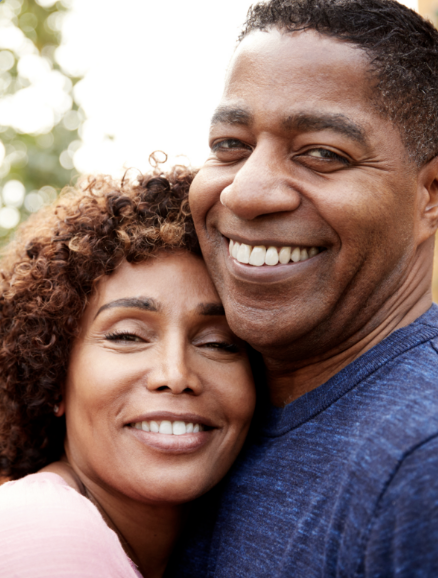Close-up of smiling African American couple embracing outdoors on a sunny day.