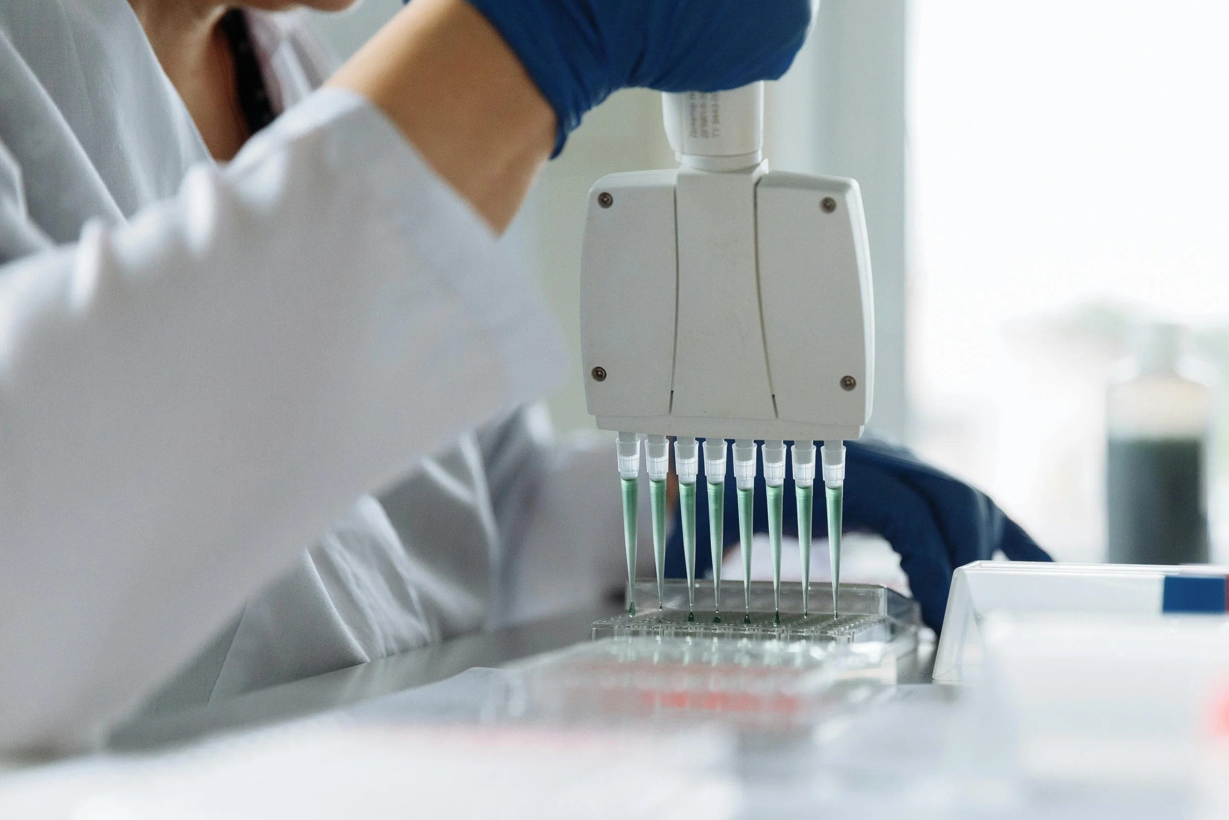 A scientist in a laboratory using a multi-channel pipette to transfer liquids into a test plate