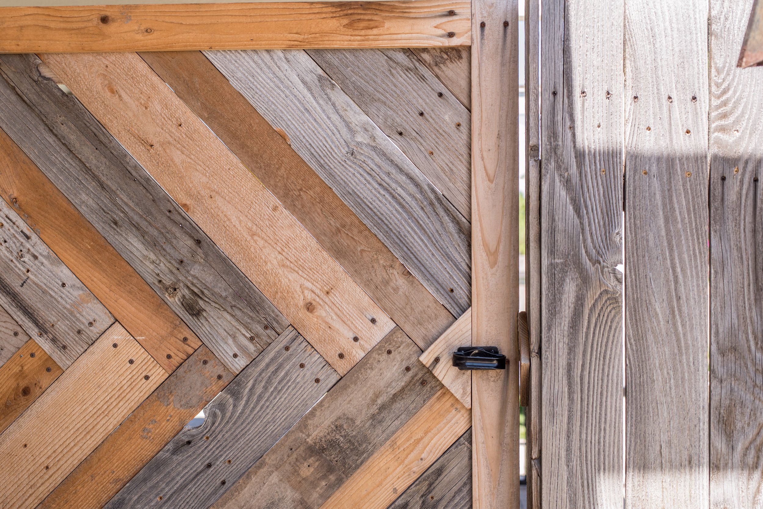 Close-up of a wooden gate made of diagonally arranged and vertically arranged weathered wood panels with a latch.