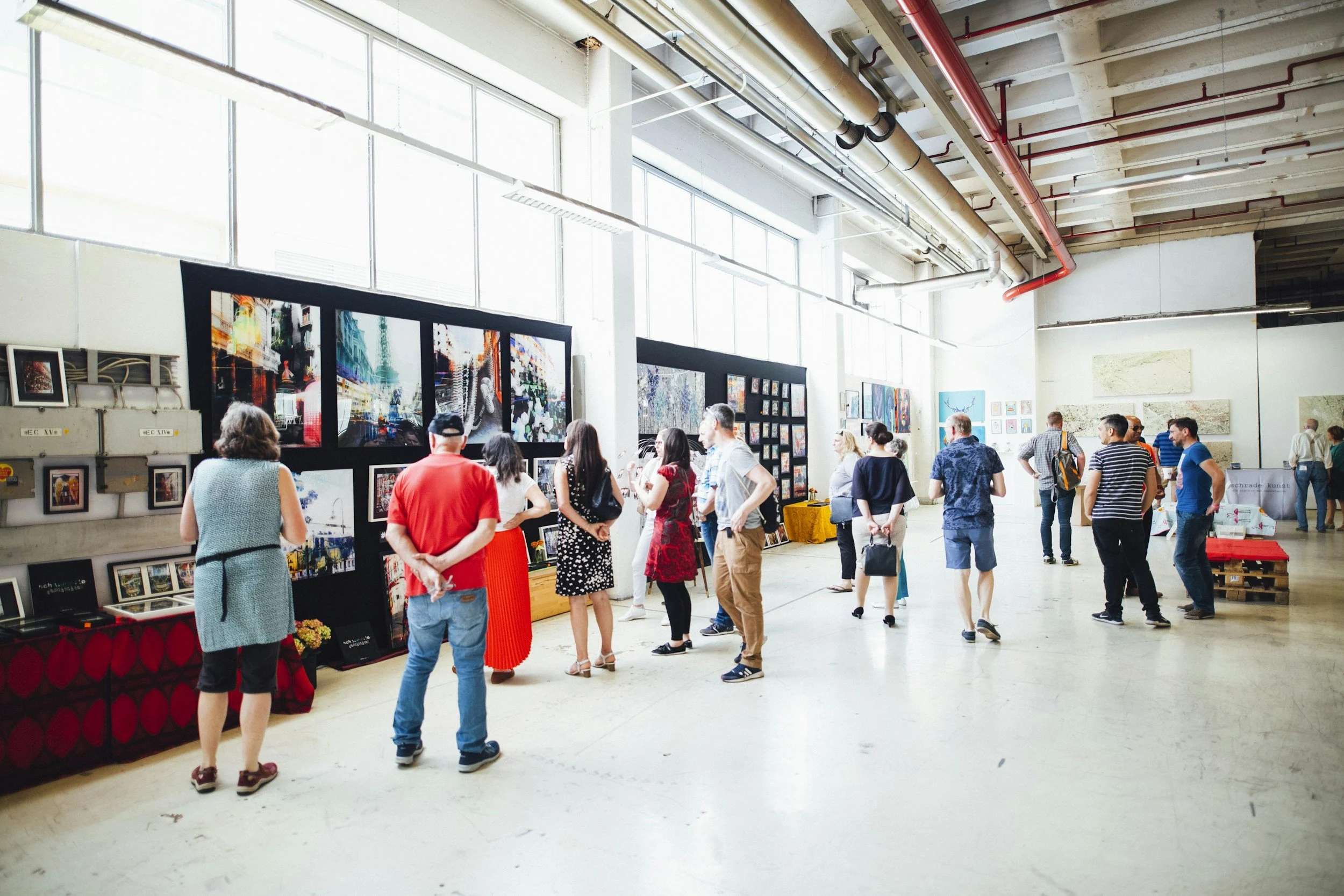 People viewing stations at an education market or exhibition in a spacious, well-lit room with large windows and high ceilings.