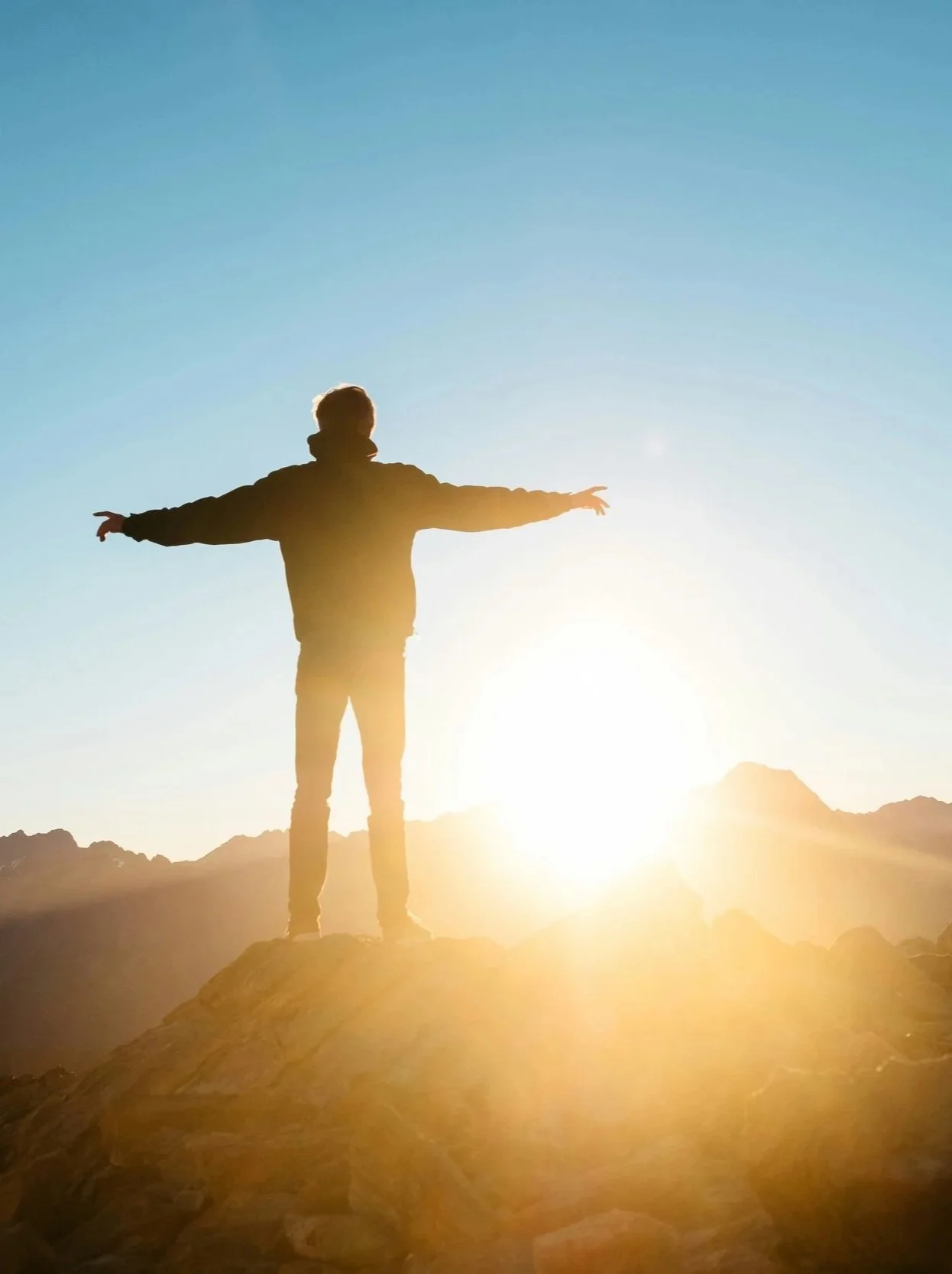 The Therapy Well - A person standing on a rocky hill with arms outstretched.