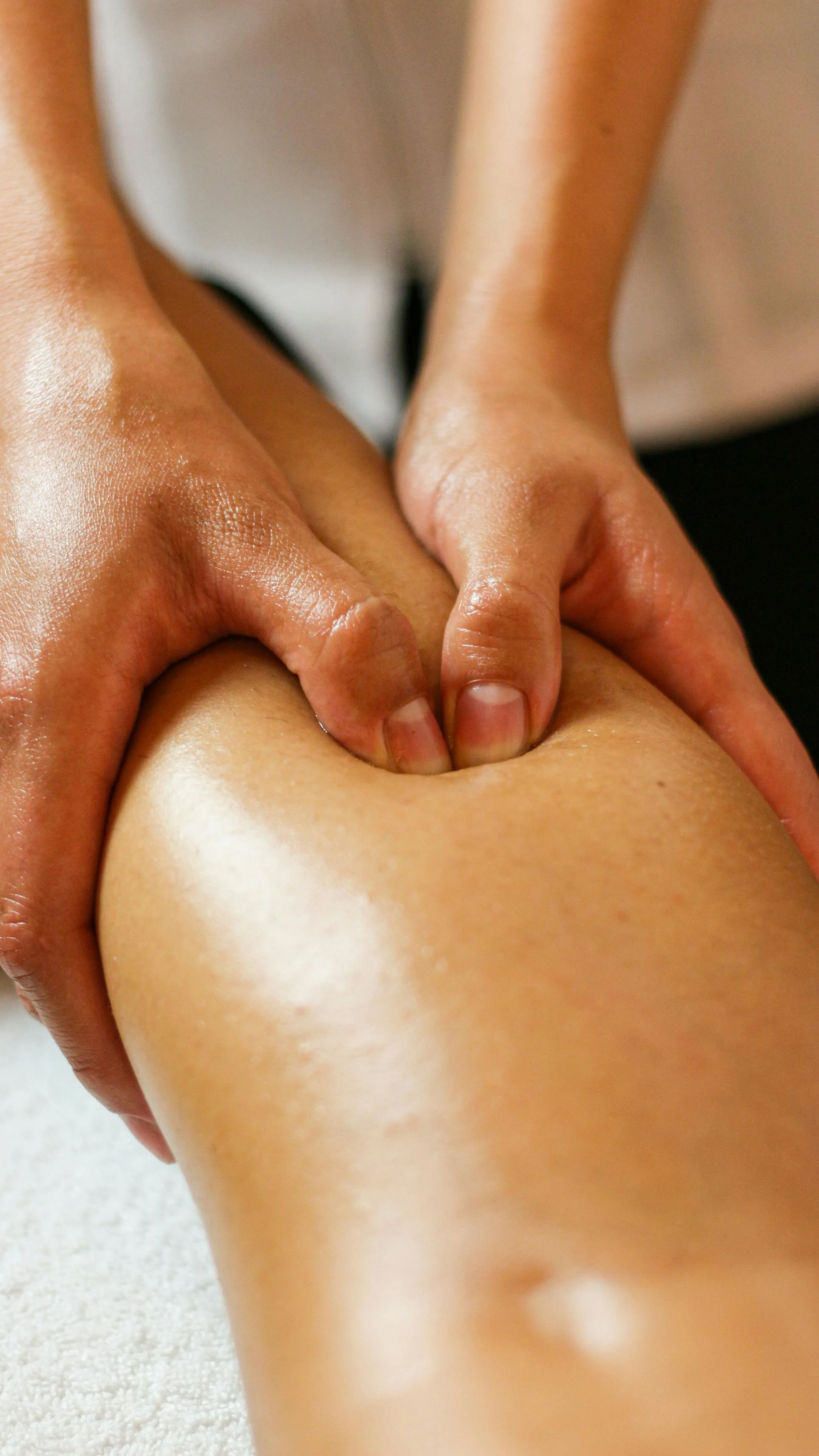 Close-up of a massage therapist applying pressure to a person's thigh during a massage.