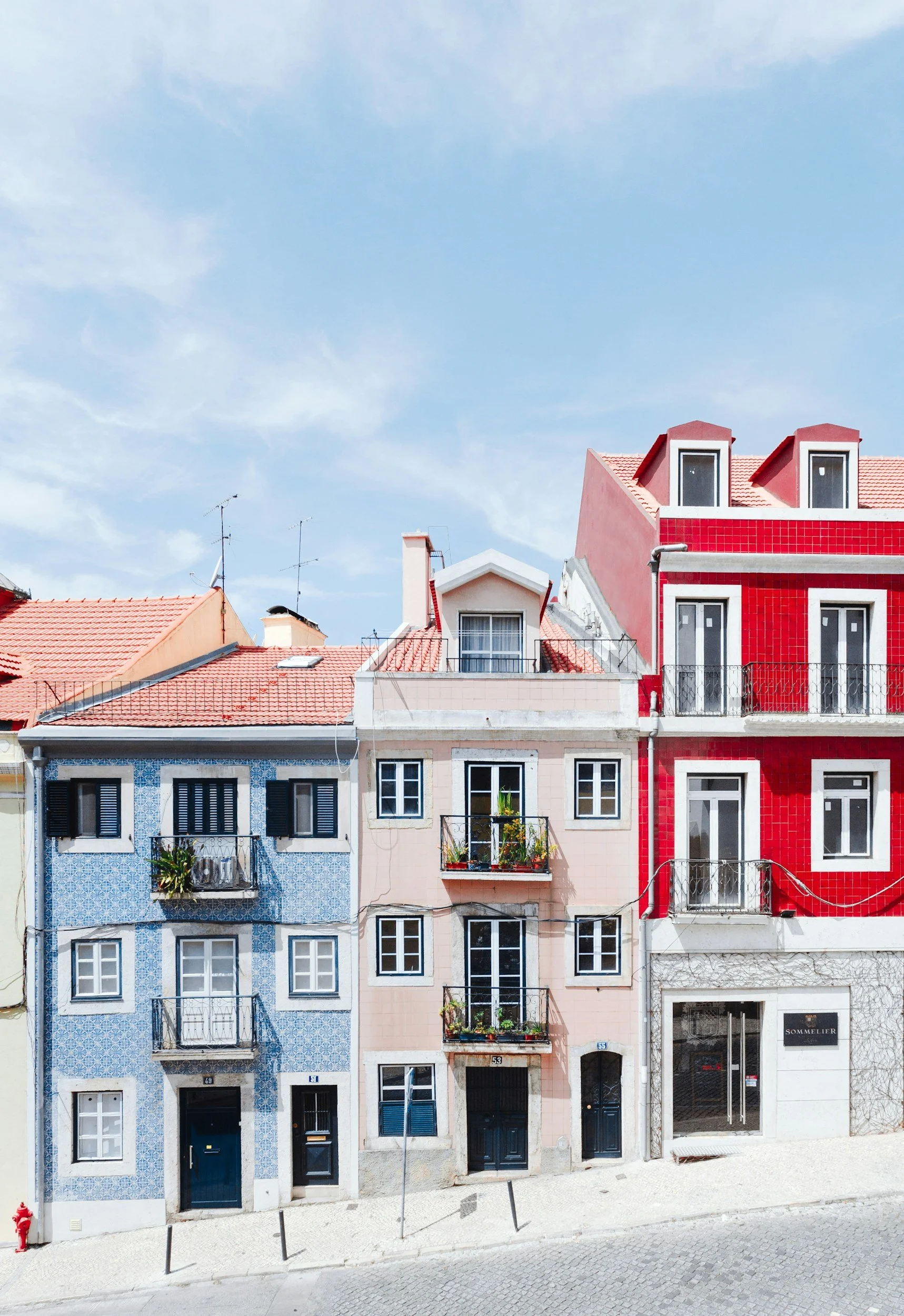 Colorful row of houses with varied designs, some with balconies and plants, under a partly cloudy sky.