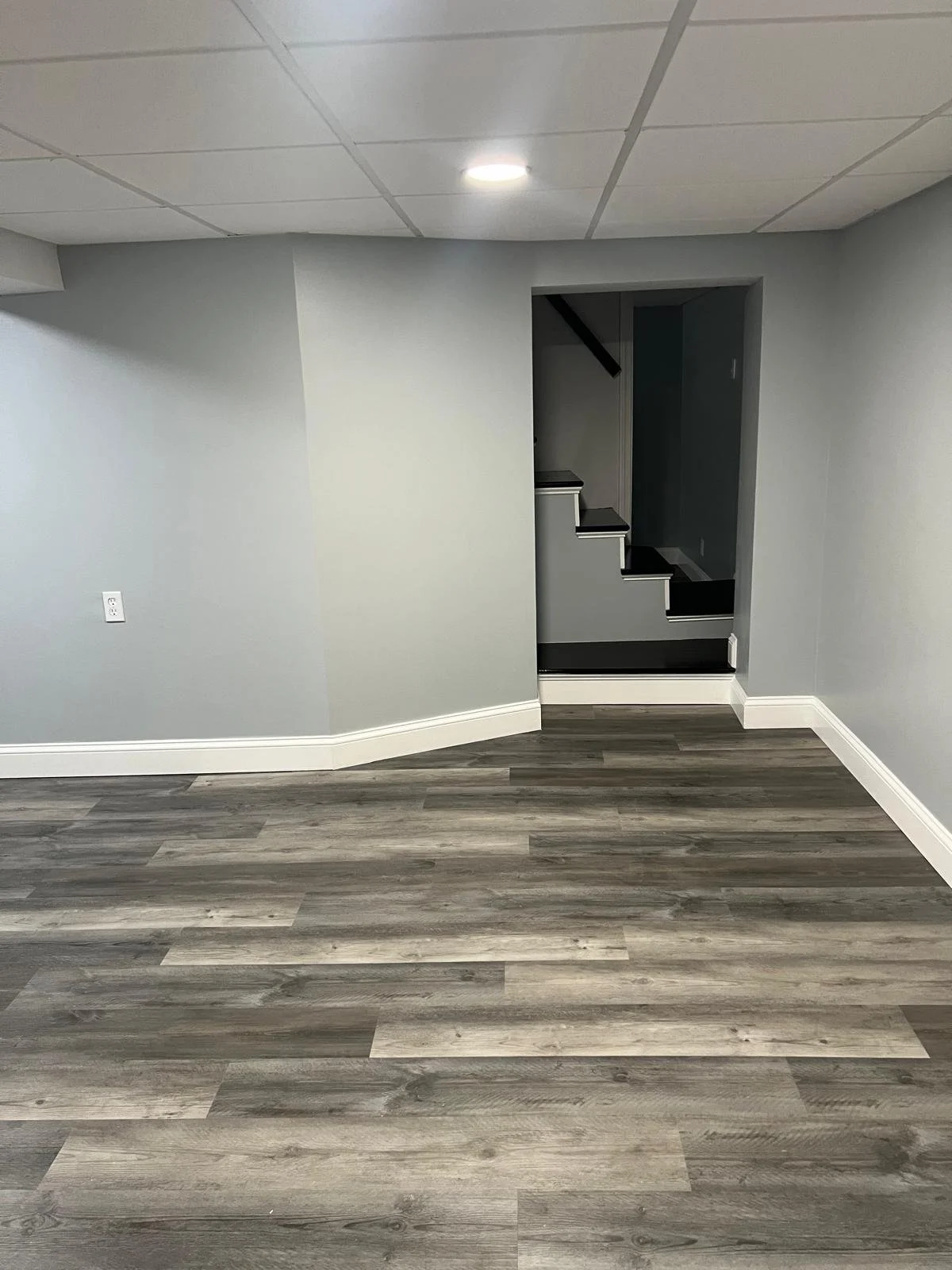 Empty room with gray walls, hardwood flooring, and a stairway leading to an upper level.