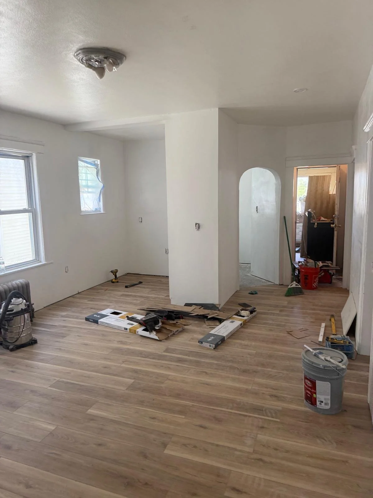 Room under renovation with newly installed wood flooring, tools, and construction materials scattered around.