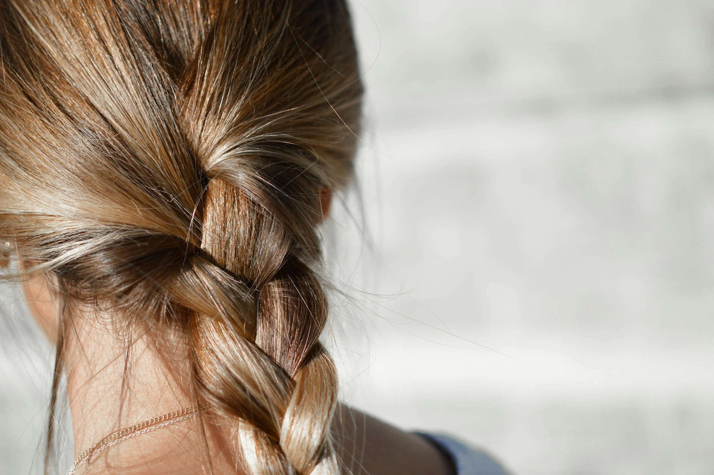 A close-up of a person's head featuring a braided hairstyle with light brown hair, with the background blurred.