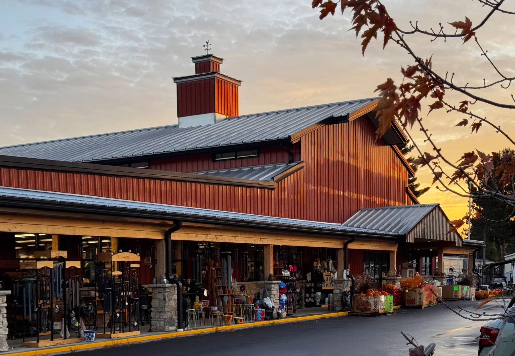 A red barn-style building with a metal roof and a chimney, featuring a display of outdoor decorations and pumpkins at sunset.