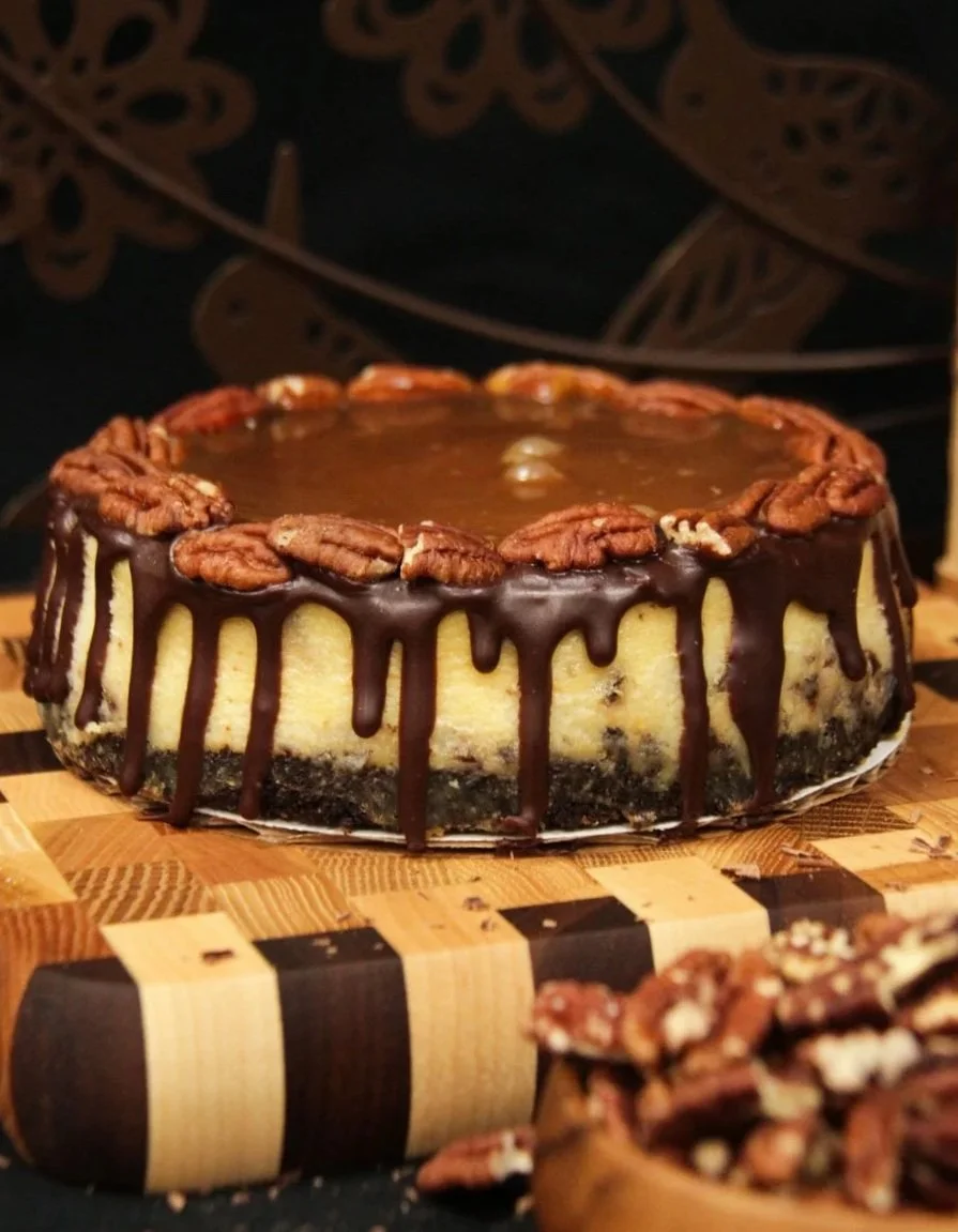 Freshly made turtle cheesecake on wooden cutting board.