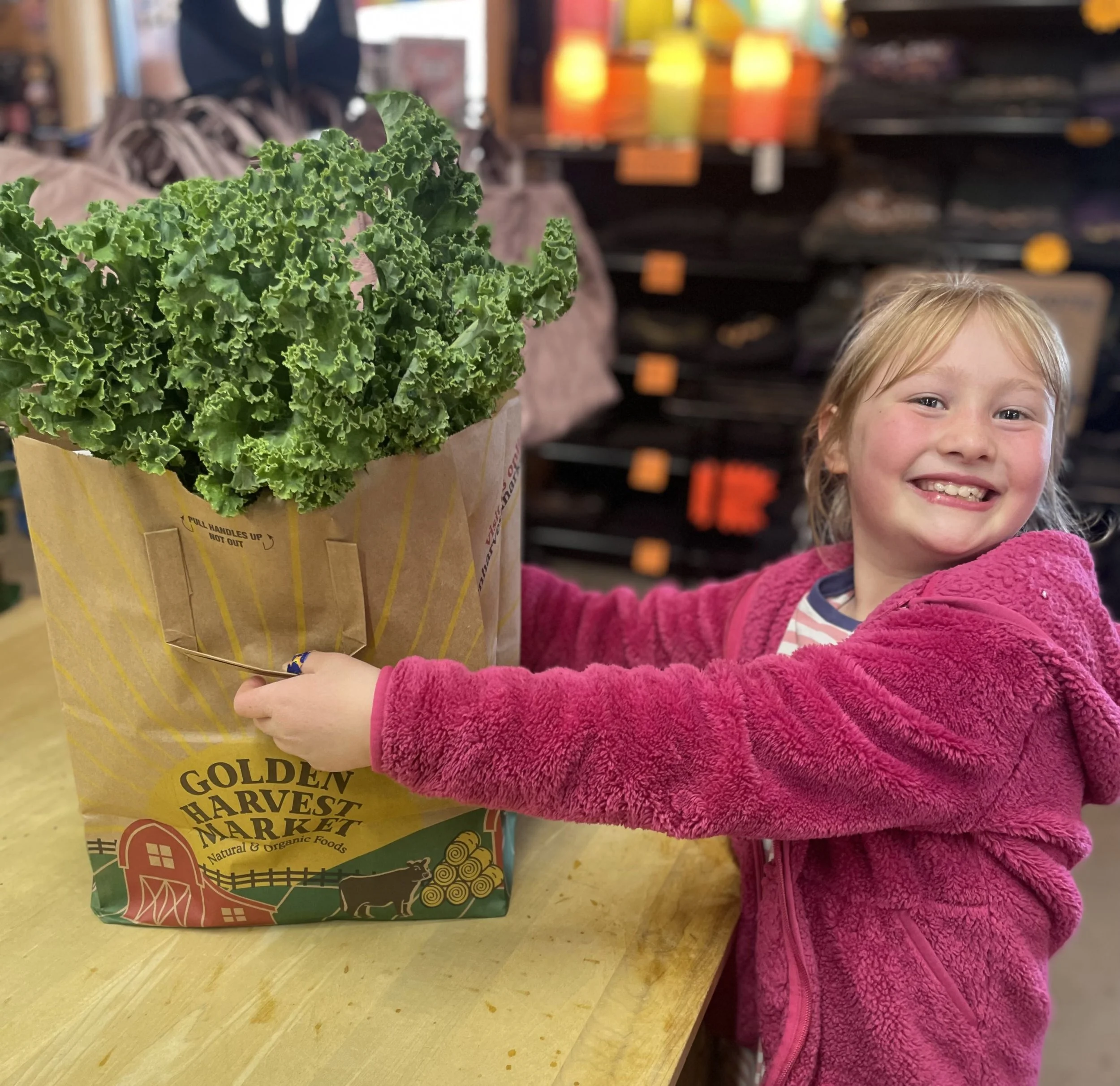 A happy customer holding a Golden Harvest paper bag filled with groceries.