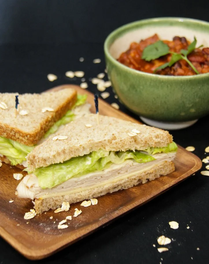 Turkey and lettuce sandwich on whole wheat bread with a bowl of chili garnished with cilantro nearby.