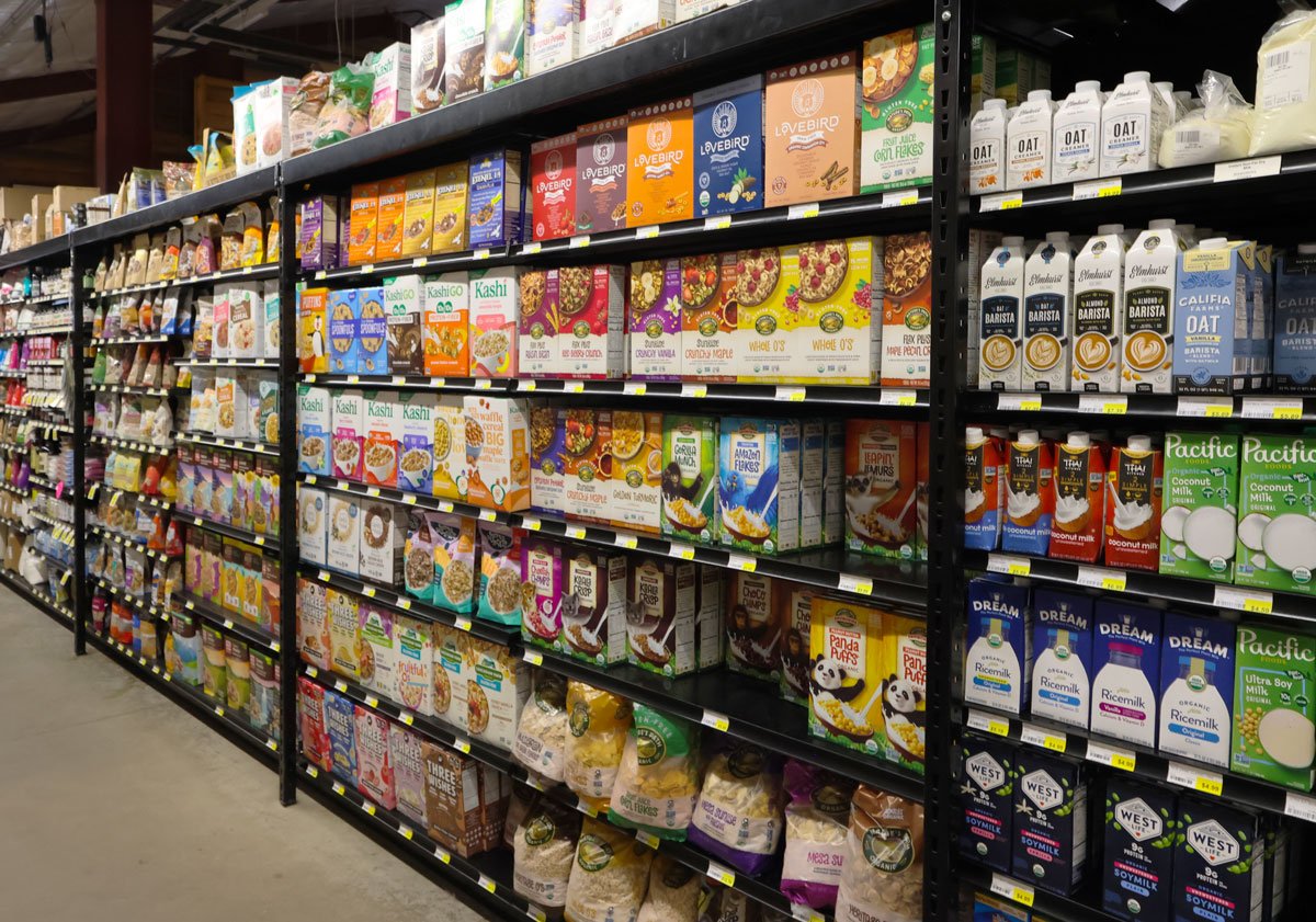 Aisle of the store with shelves stocked with various brands of cereal, oatmeal, and plant-based milk.