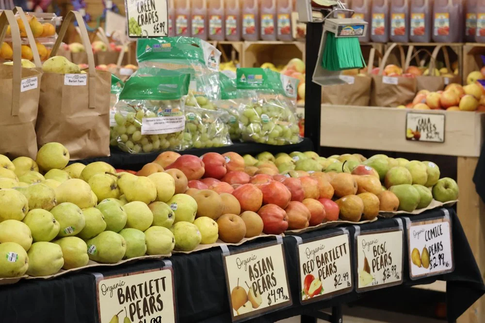 Display of organic pears, including Bartlett, Asian, Red Bartlett, Bosc, and Comice varieties, arranged on a produce stand at a grocery store.