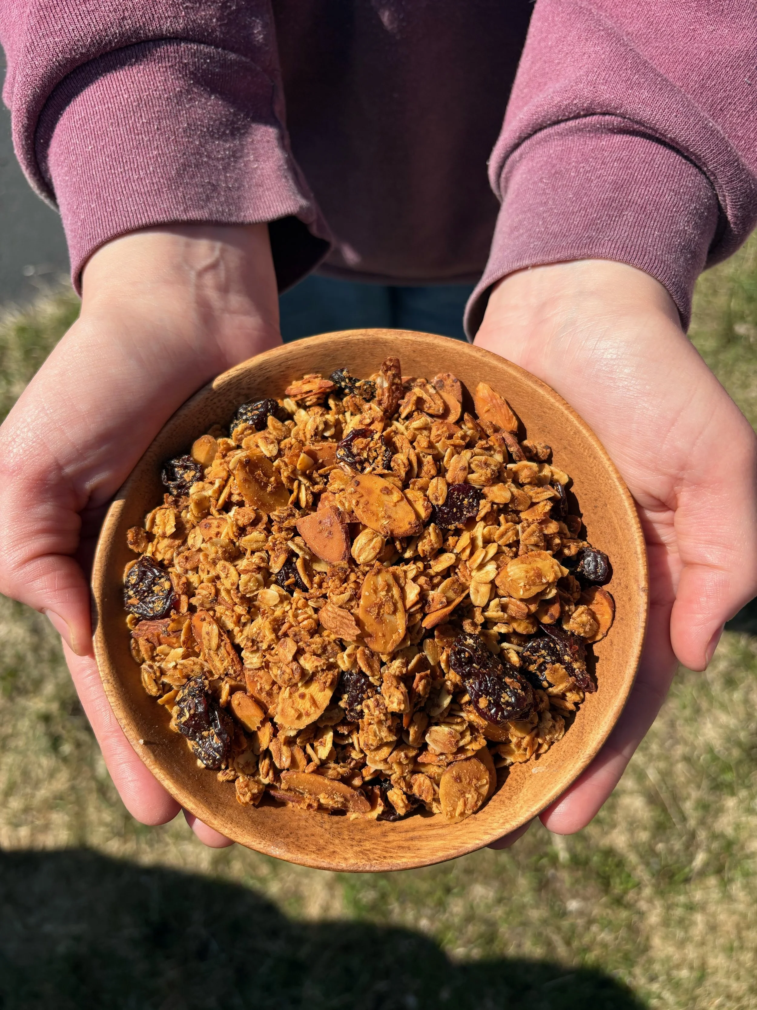 Hands holding freshly made granola in a wooden bowl.