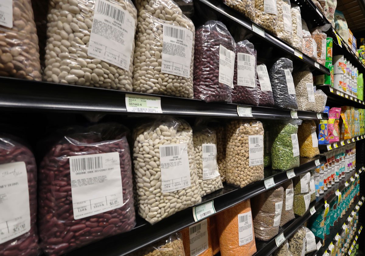 Shelves stocked with plastic bags of various dry beans in a grocery store.