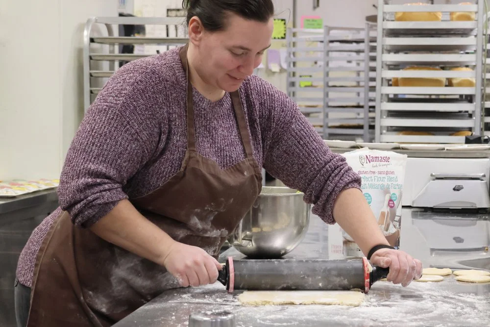 Woman rolling out cookie dough with a rolling pin in a bakery kitchen.