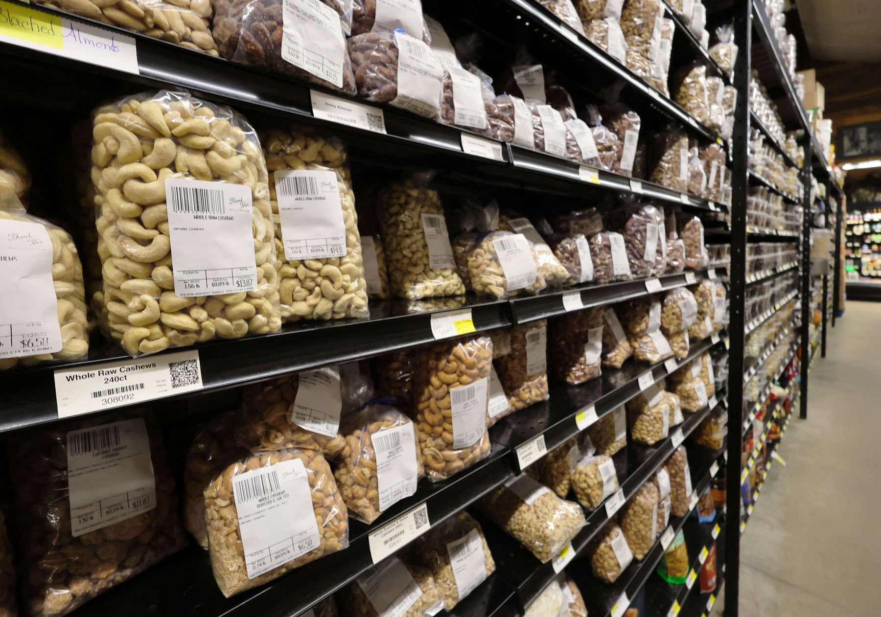Shelves filled with bags of mixed nuts, including cashews, almonds, and other varieties in a grocery store.