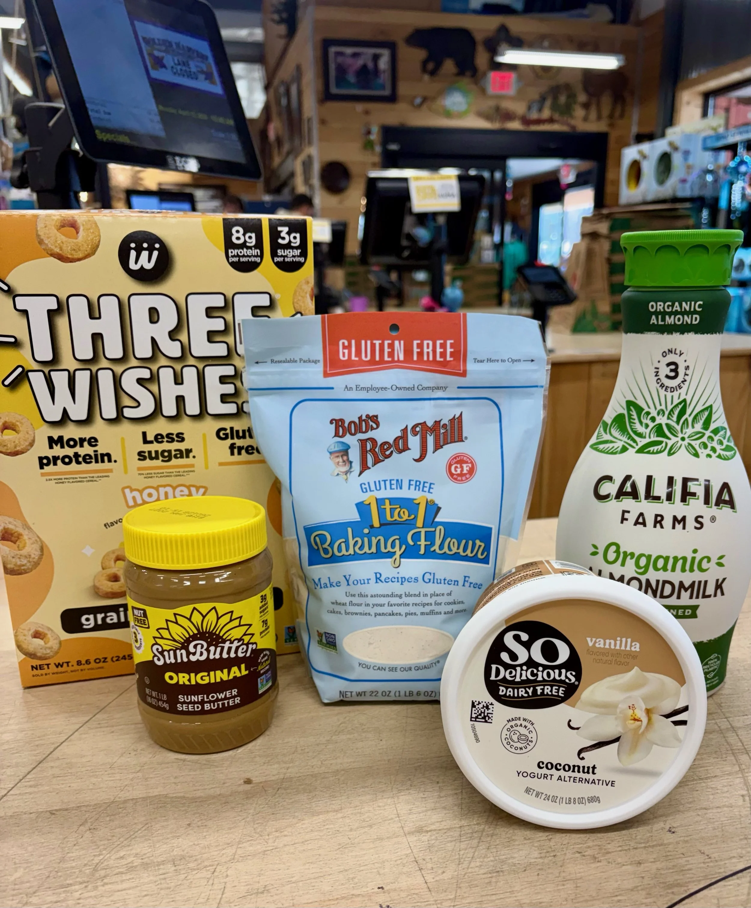 Specialty diet grocery items featuring dairy free almond milk and coconut yogurt, gluten free flour and cereal, and sunflower seed butter.