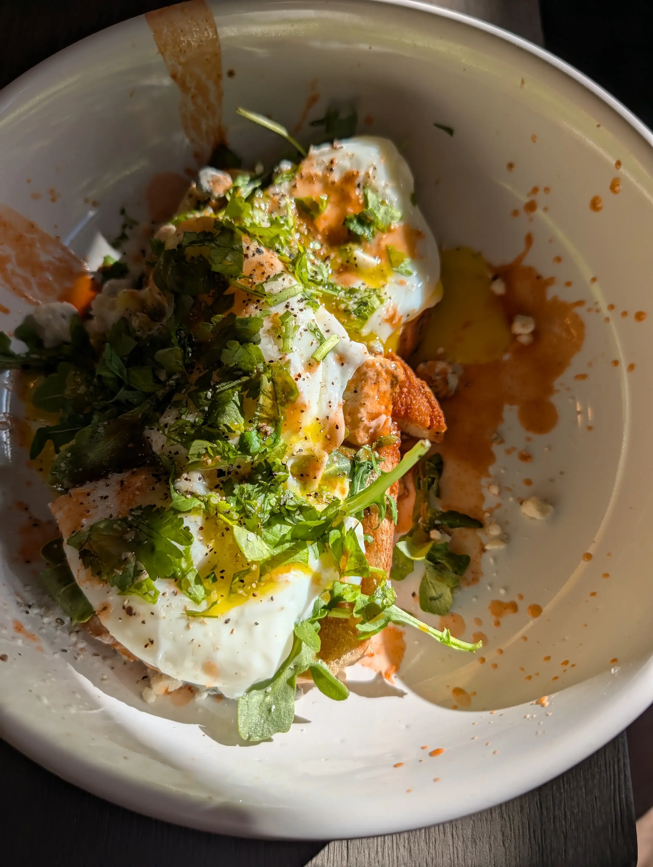 Poached eggs topped with chopped herbs and black pepper, served on toast with some sauce or seasoning, in a white bowl.