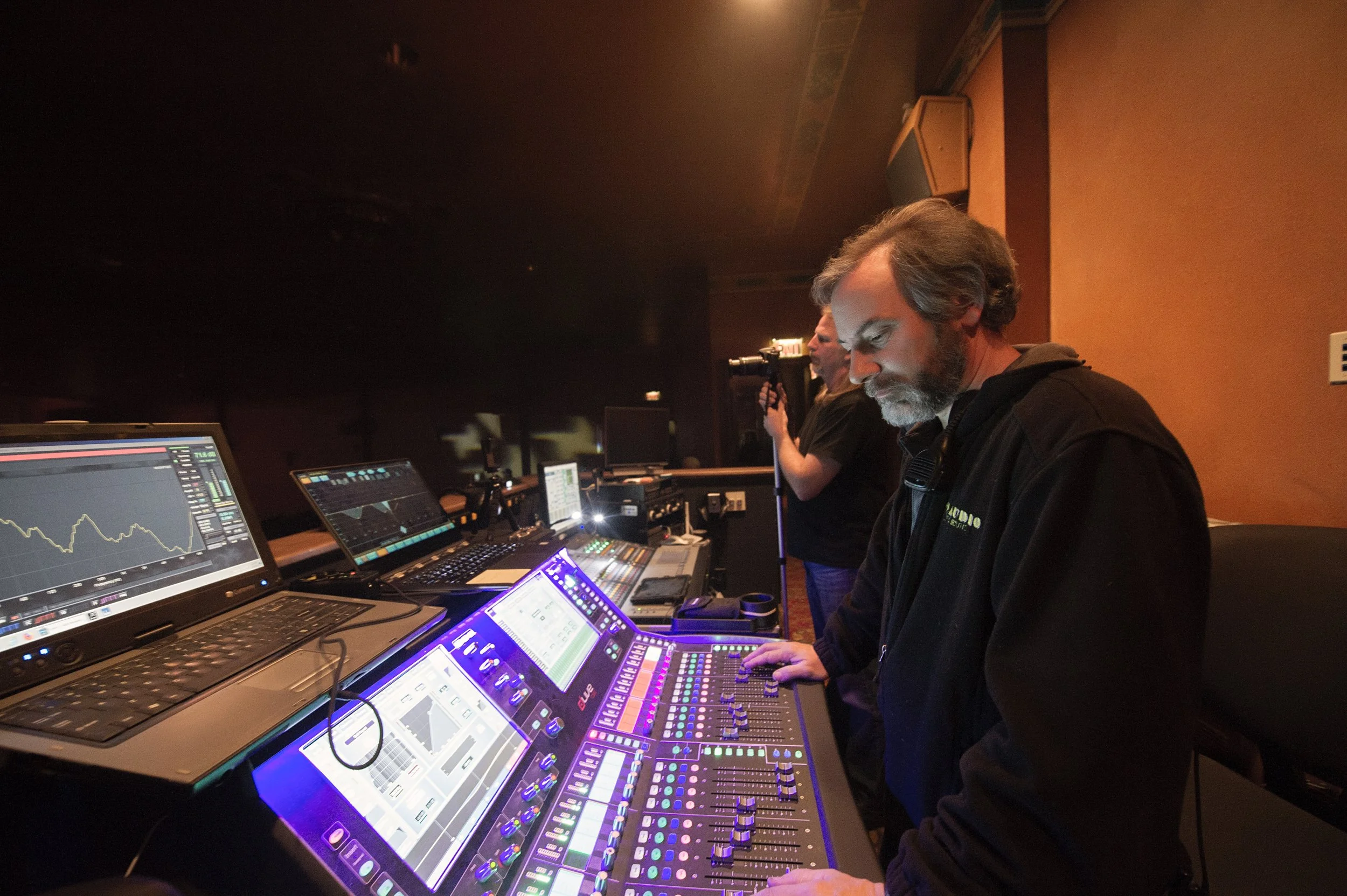 Two men working with mixing consoles and monitors in a dark sound studio.