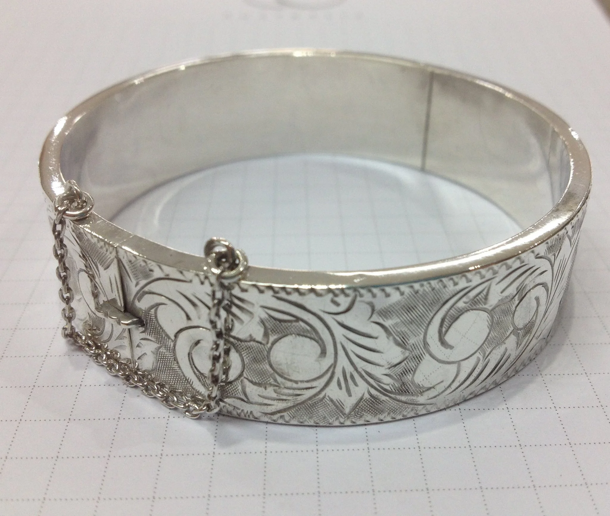 Close-up of a silver decorative bracelet or bangle with intricate engraved patterns and chained accents.