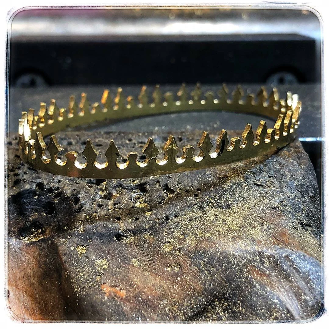 A gold pierced bezel crown resting on a dark, speckled rock surface.
