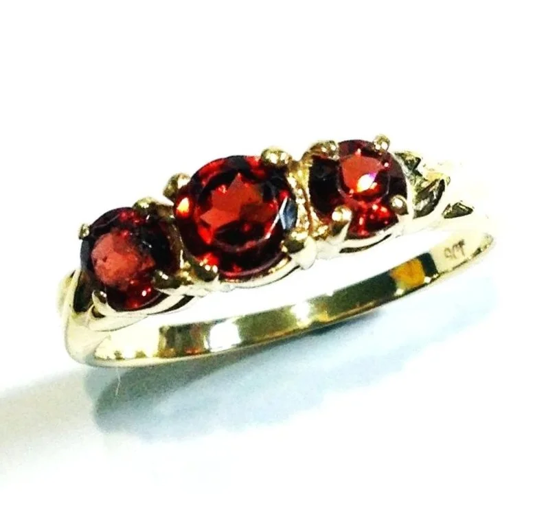 Gold ring with three red gemstones set in a row, possibly garnets or rubies.