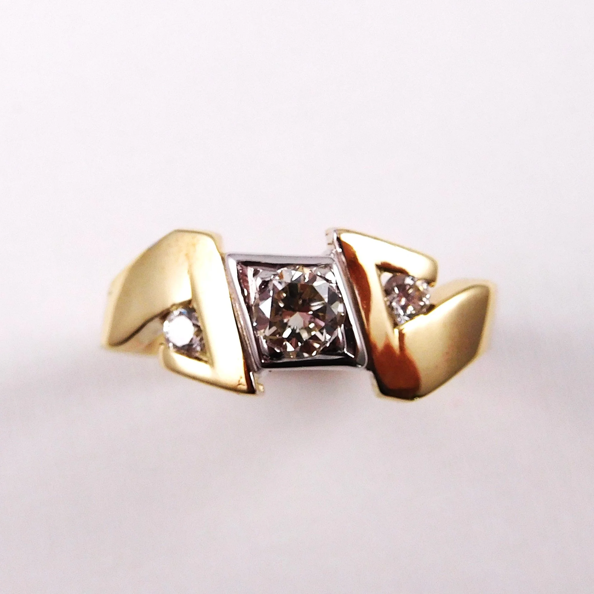 Close-up of a gold ring with a square-shaped setting containing a dark gemstone, accompanied by three smaller round gemstones on a white background.