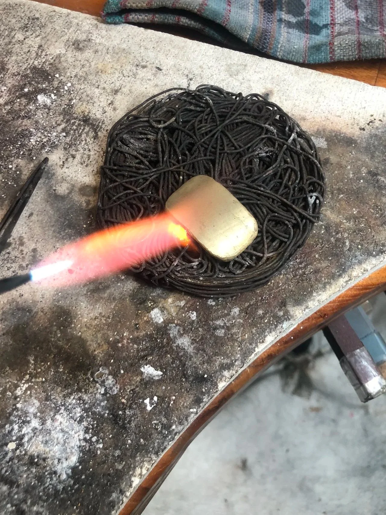 A piece of gold, with a flame from a torch heating the metal.