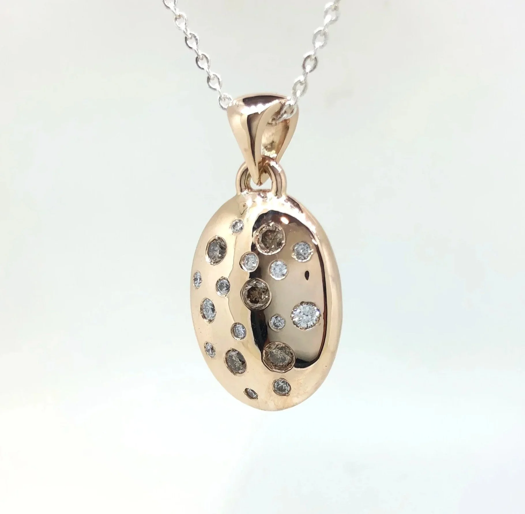 Close-up of an oval gold pendant, adorned with numerous small, sparkling diamonds. 