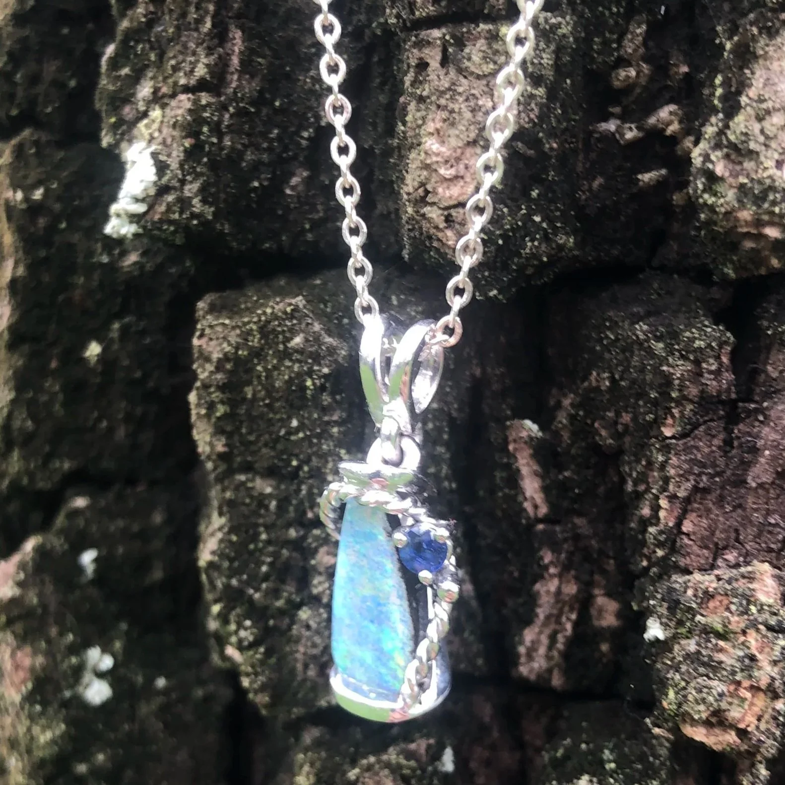 Opal pendant hanging against a rough, textured rock wall outdoors.