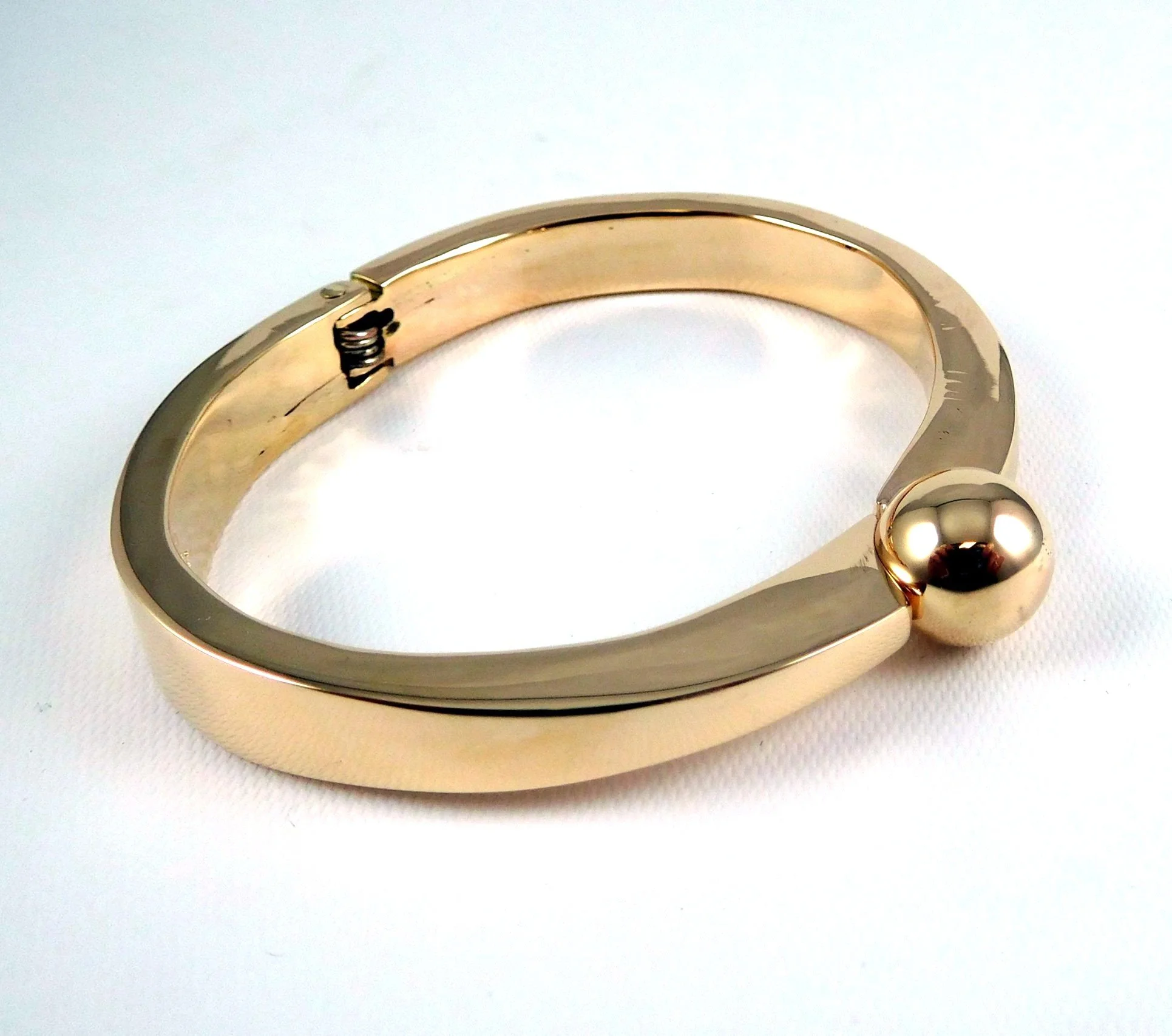 A close-up photo of a hinged gold bracelet featuring a spherical ornament.