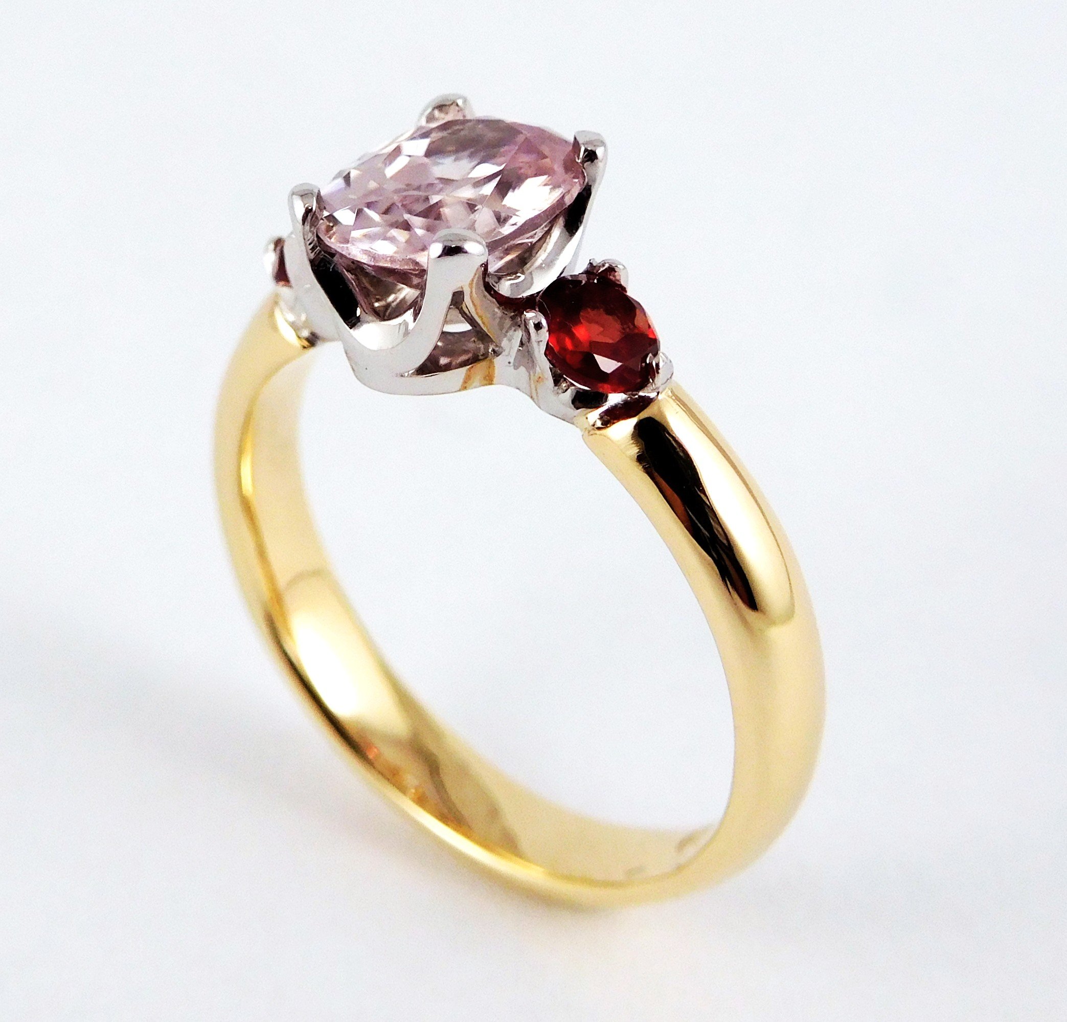 Close-up of a ring with a large pink gemstone and a smaller red gemstone on a gold band.