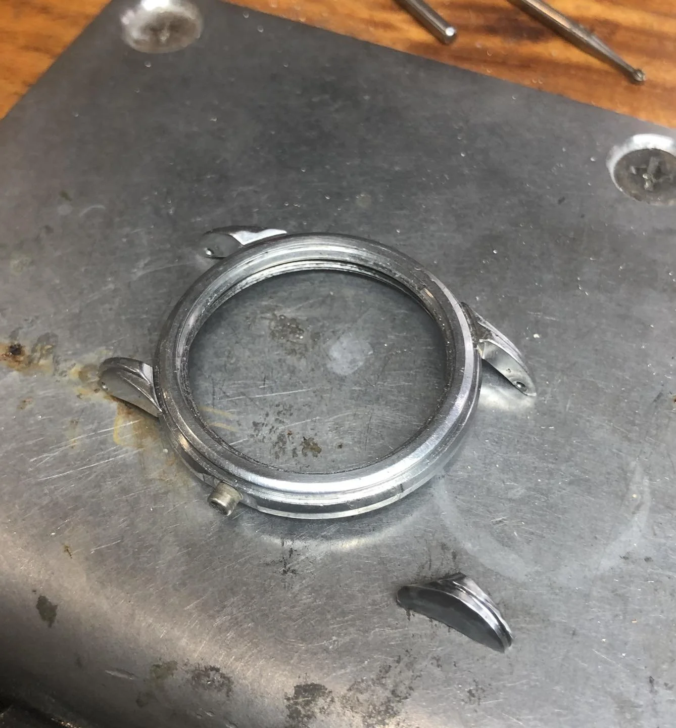A watch case with no watch inside, placed on a workbench with tools nearby.