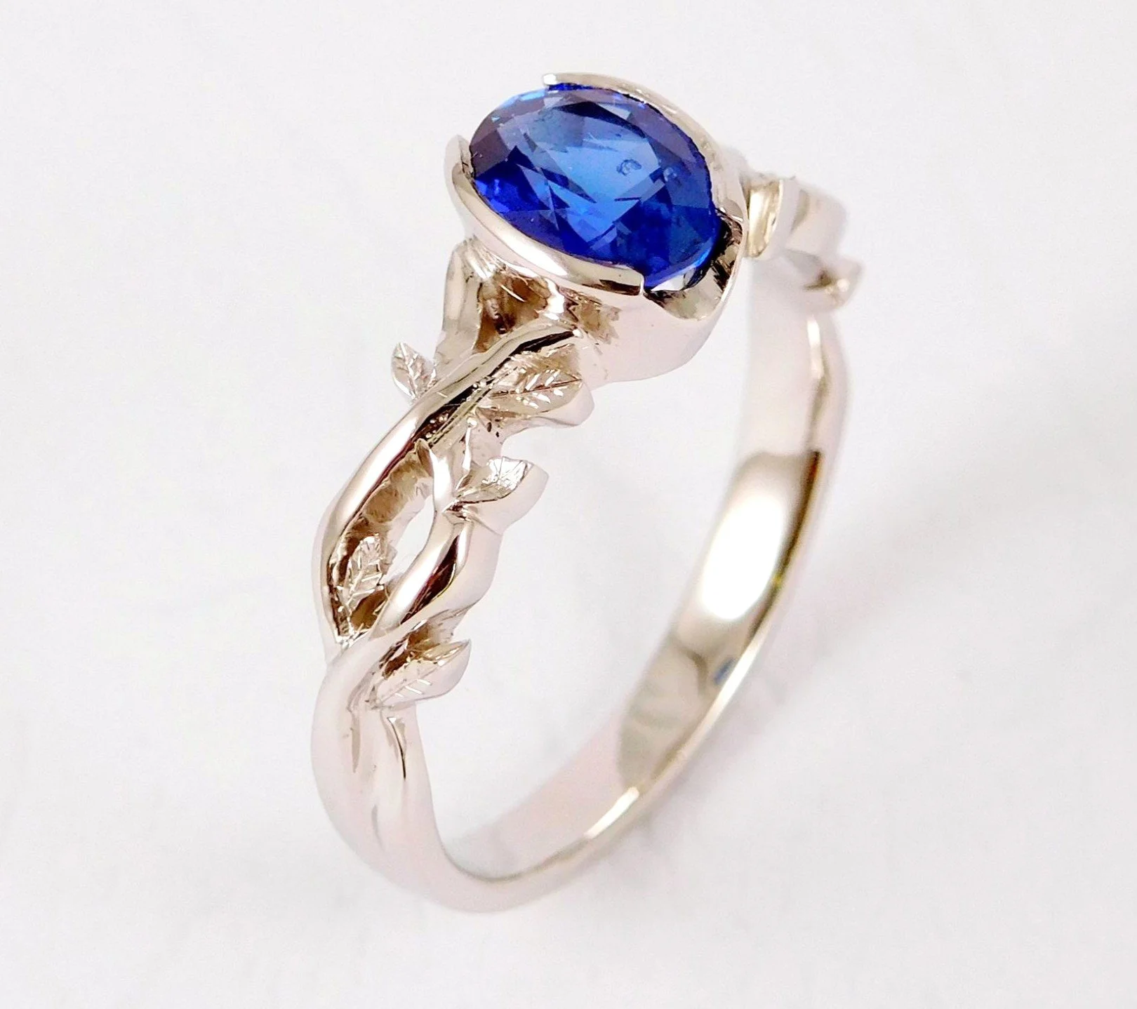 White gold ring with a large, teardrop-shaped blue sapphire gemstone and intricate leaf-like designs on the band.