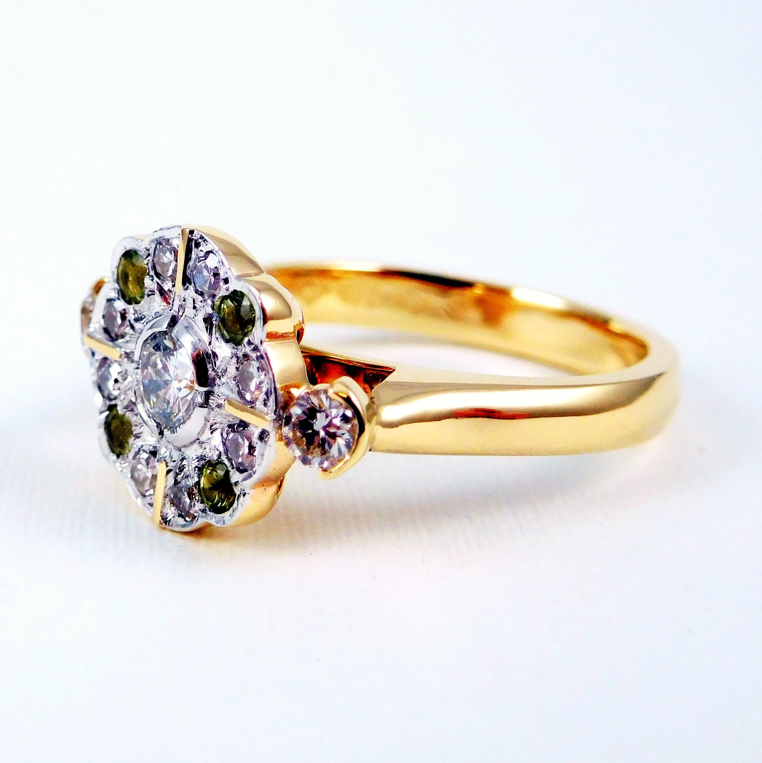Close-up of a gold ring with a cluster of small diamonds and green gemstones set in a flower shape.