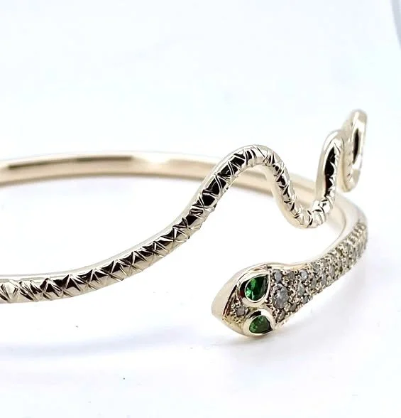 Close-up of a gold snake-shaped bracelet with emeralds and diamonds on its head.