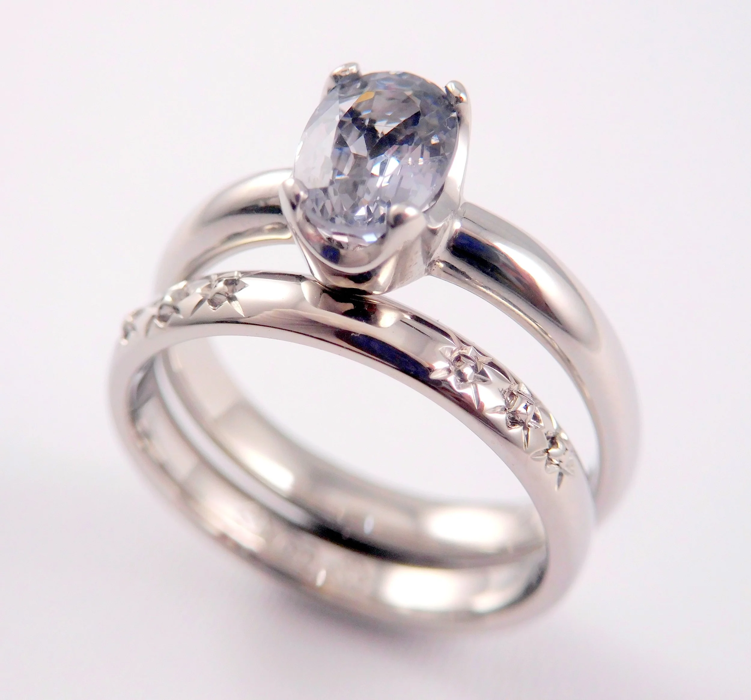 A white gold ring with a large oval-cut clear gemstone, set in prongs on a plain band. With a matching wedding ring. 