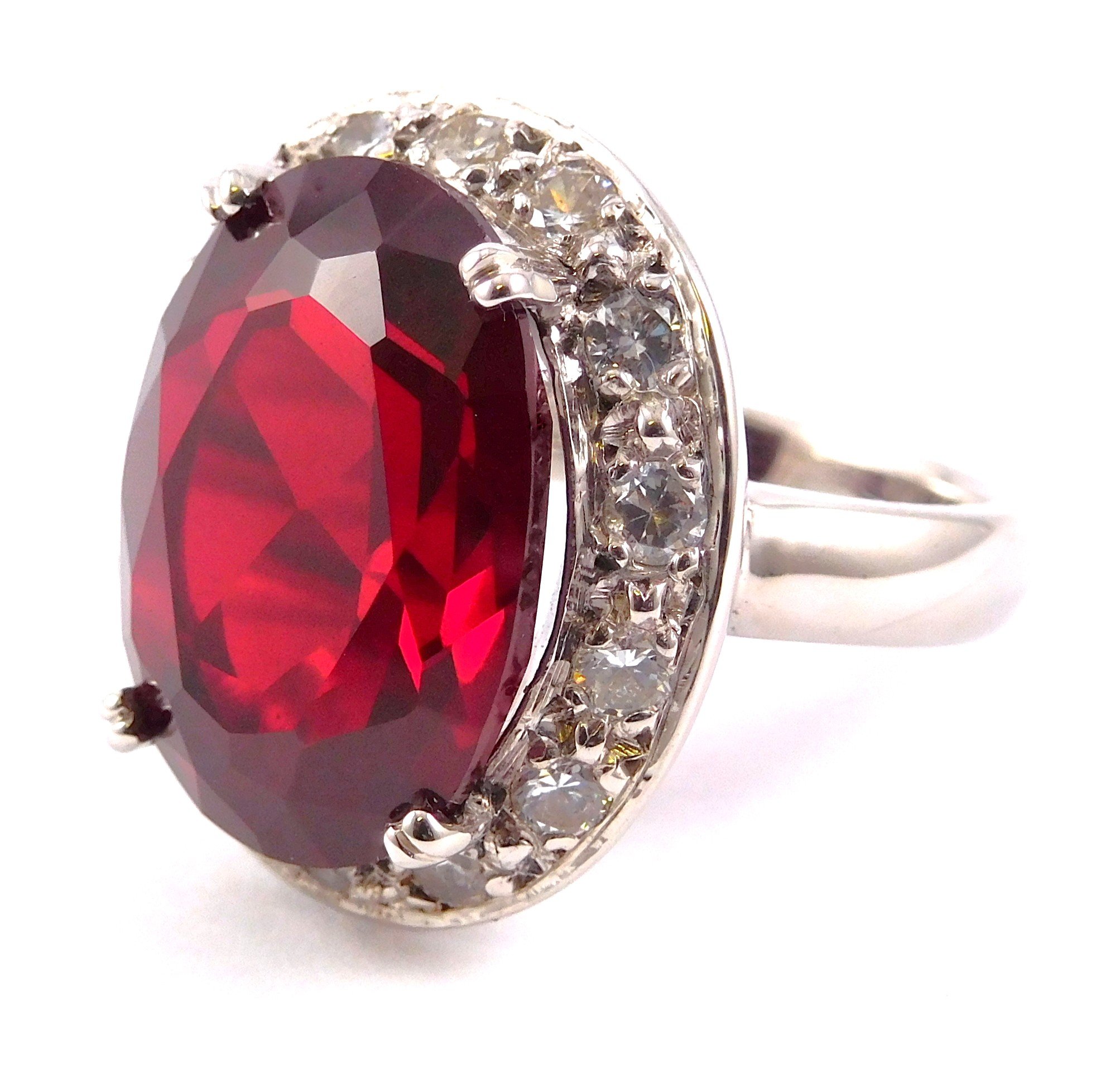 Close-up of a ring with a large red gemstone and surrounded by smaller clear gemstones on a white background.