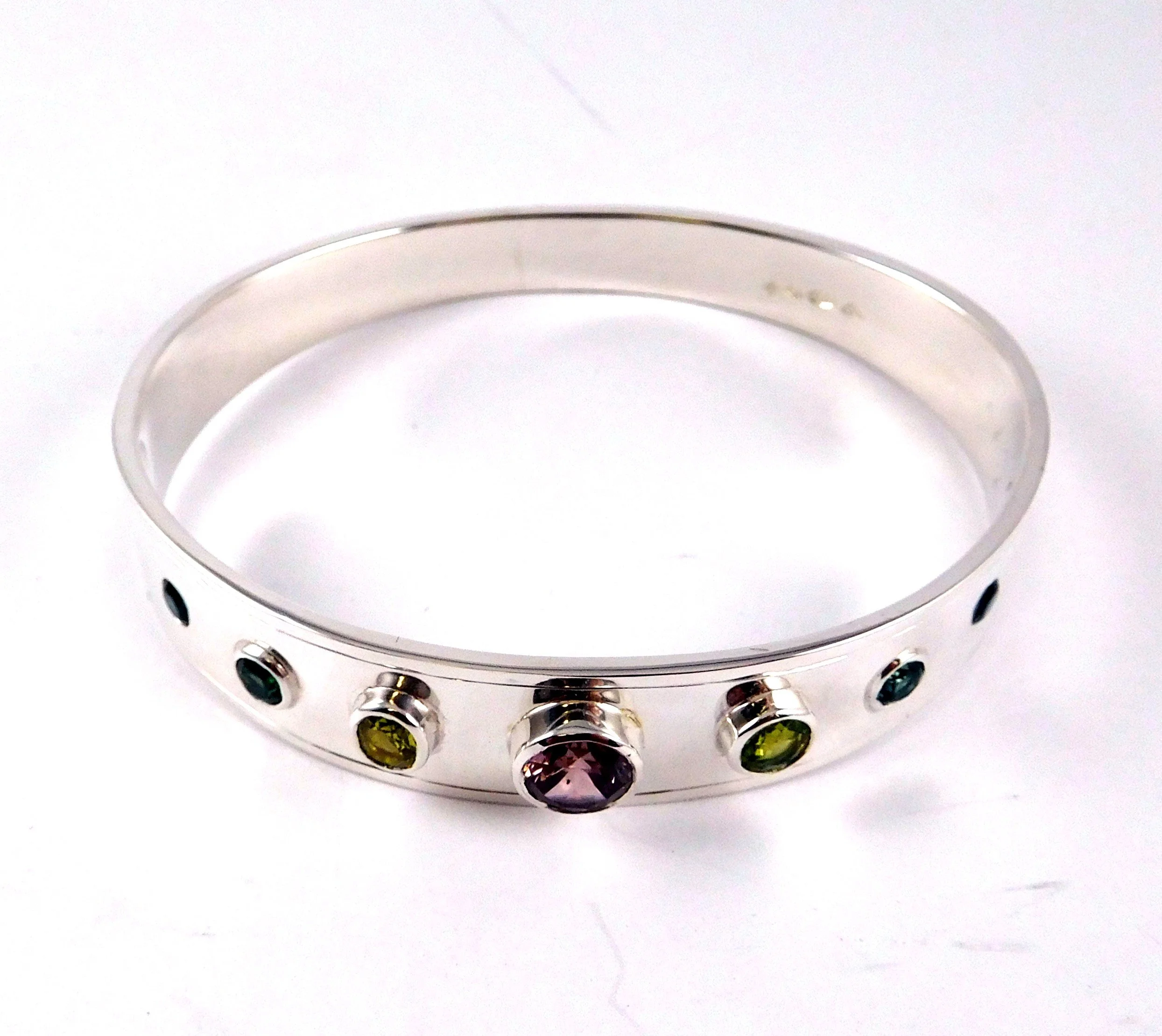 A sterling silver bangle with multiple colorful gemstones embedded around its circumference.