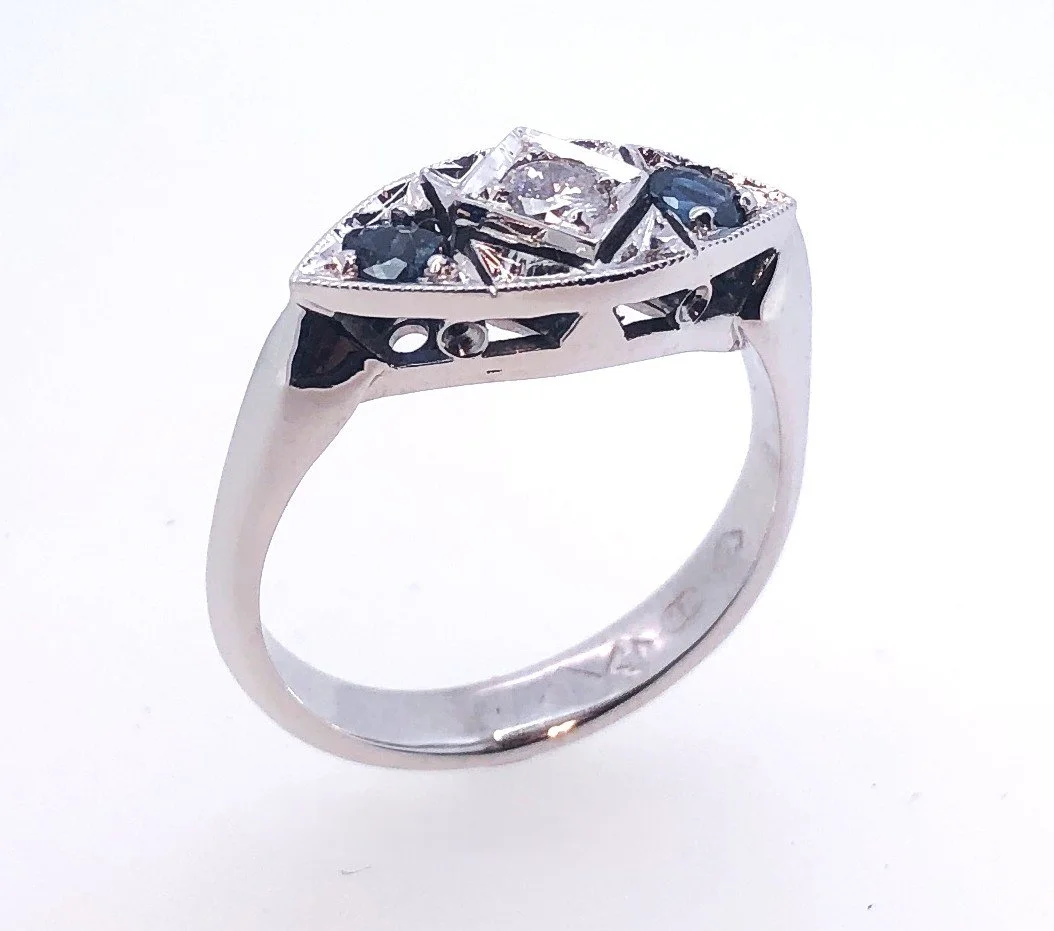 A silver ring with a rectangular clear gemstone in the center, surrounded by smaller black and clear stones, set in an intricate design.