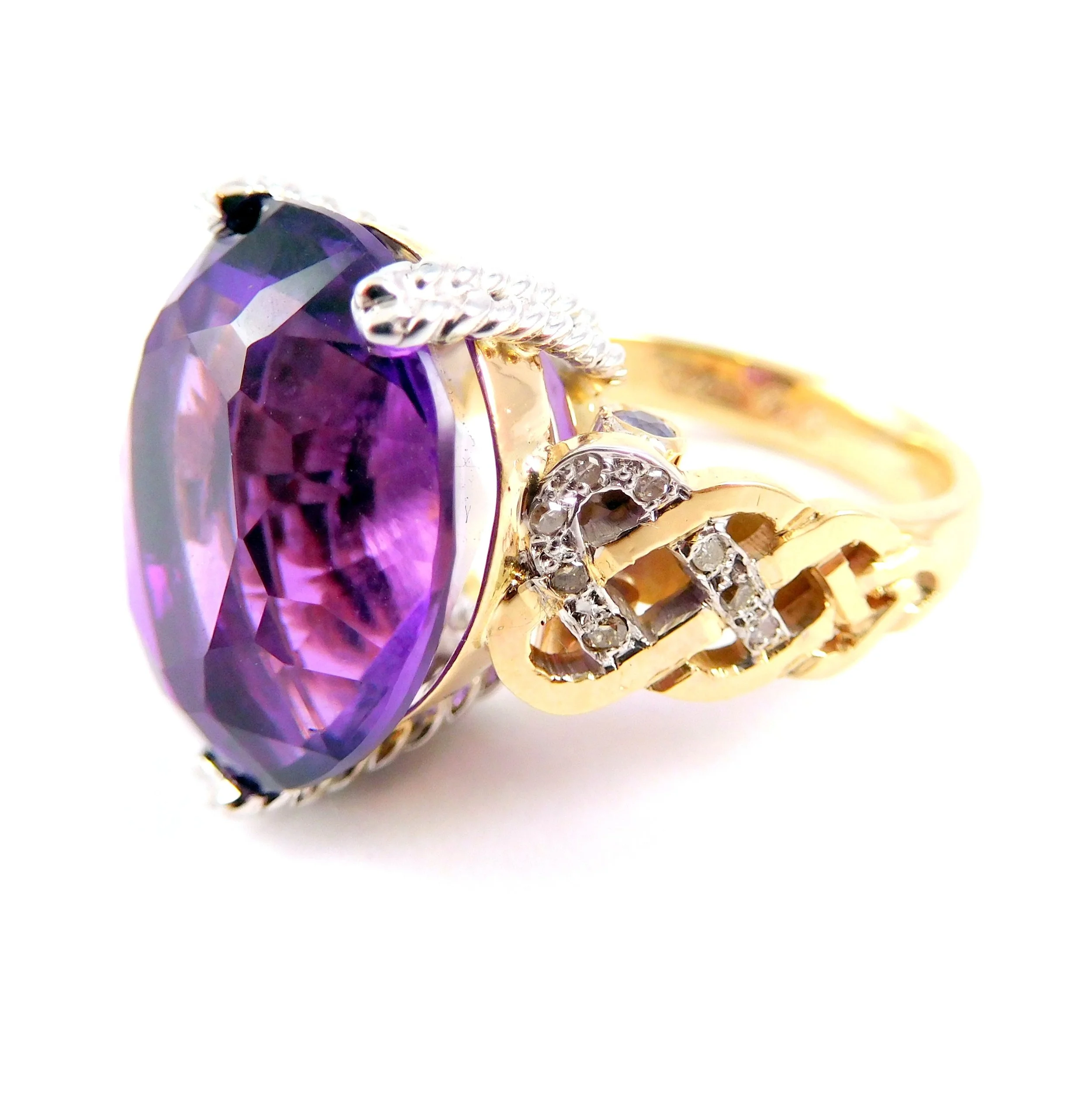 Close-up of a ring featuring a large purple gemstone, surrounded by smaller clear stones and set in a gold band.