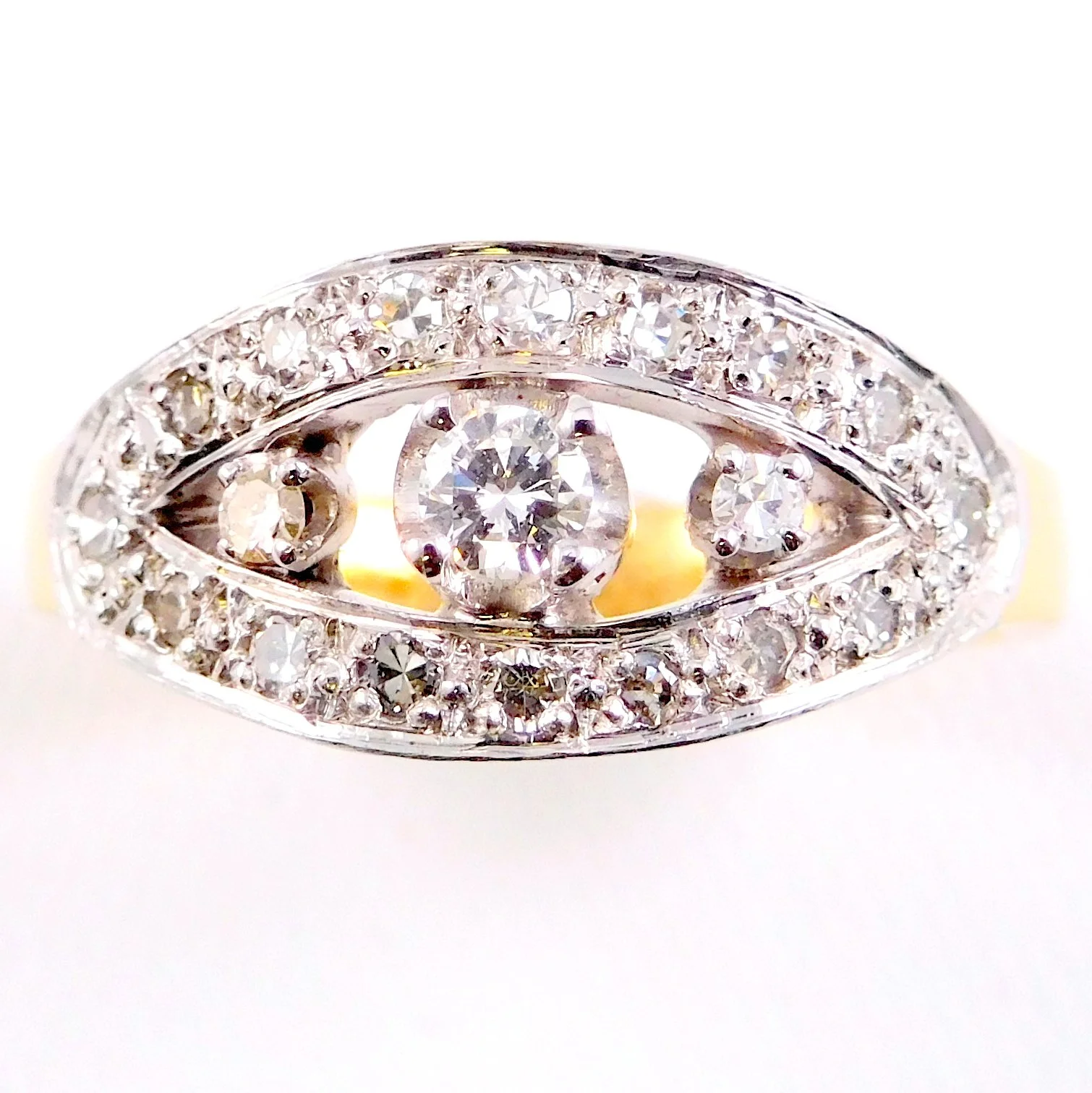 A close-up of a diamond ring with a central round diamond surrounded by small diamonds on a white background.