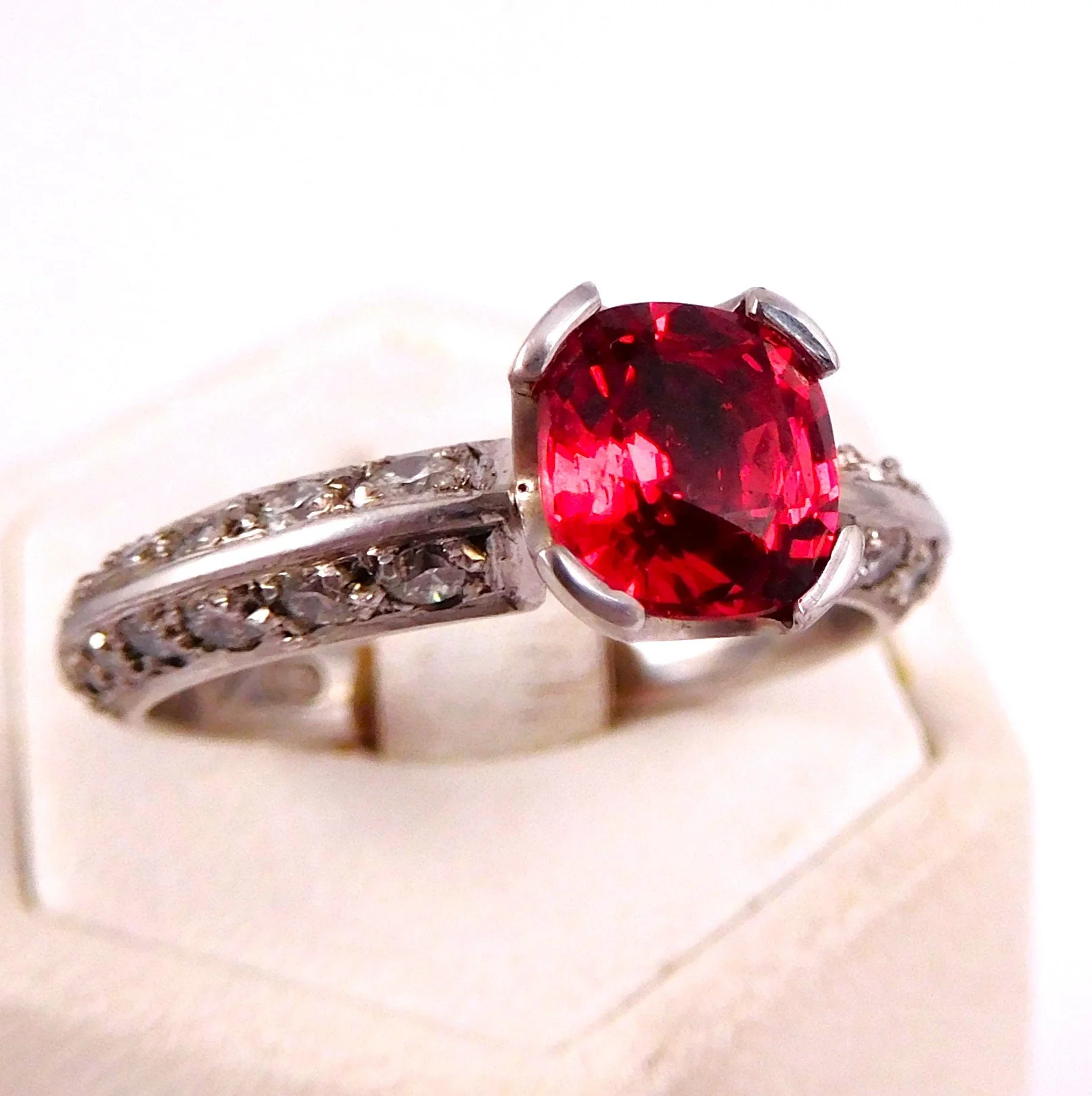 Close-up of a silver ring with a large red gemstone in the center and smaller clear stones along the band.